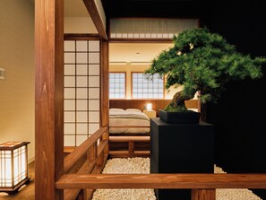 A traditional Japanese-style room with tatami flooring, a low wooden bed, a bonsai tree, and a shoji screen.