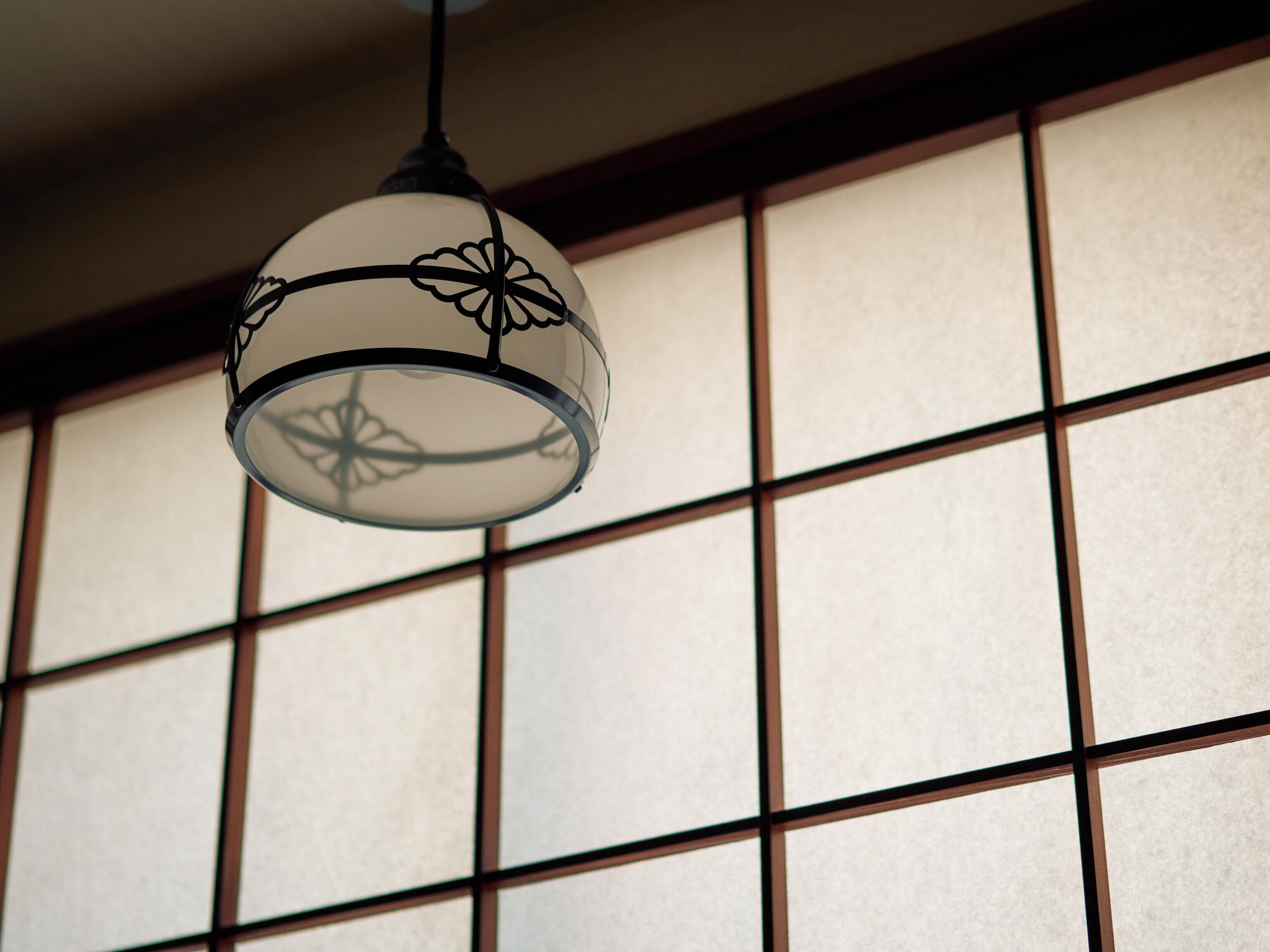 A hanging lamp with a floral design against a background of a room with a grid-patterned wall.