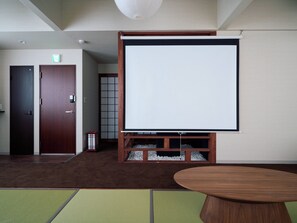 A room with a large white projection screen, a wooden door, a small table, and a tatami mat floor.