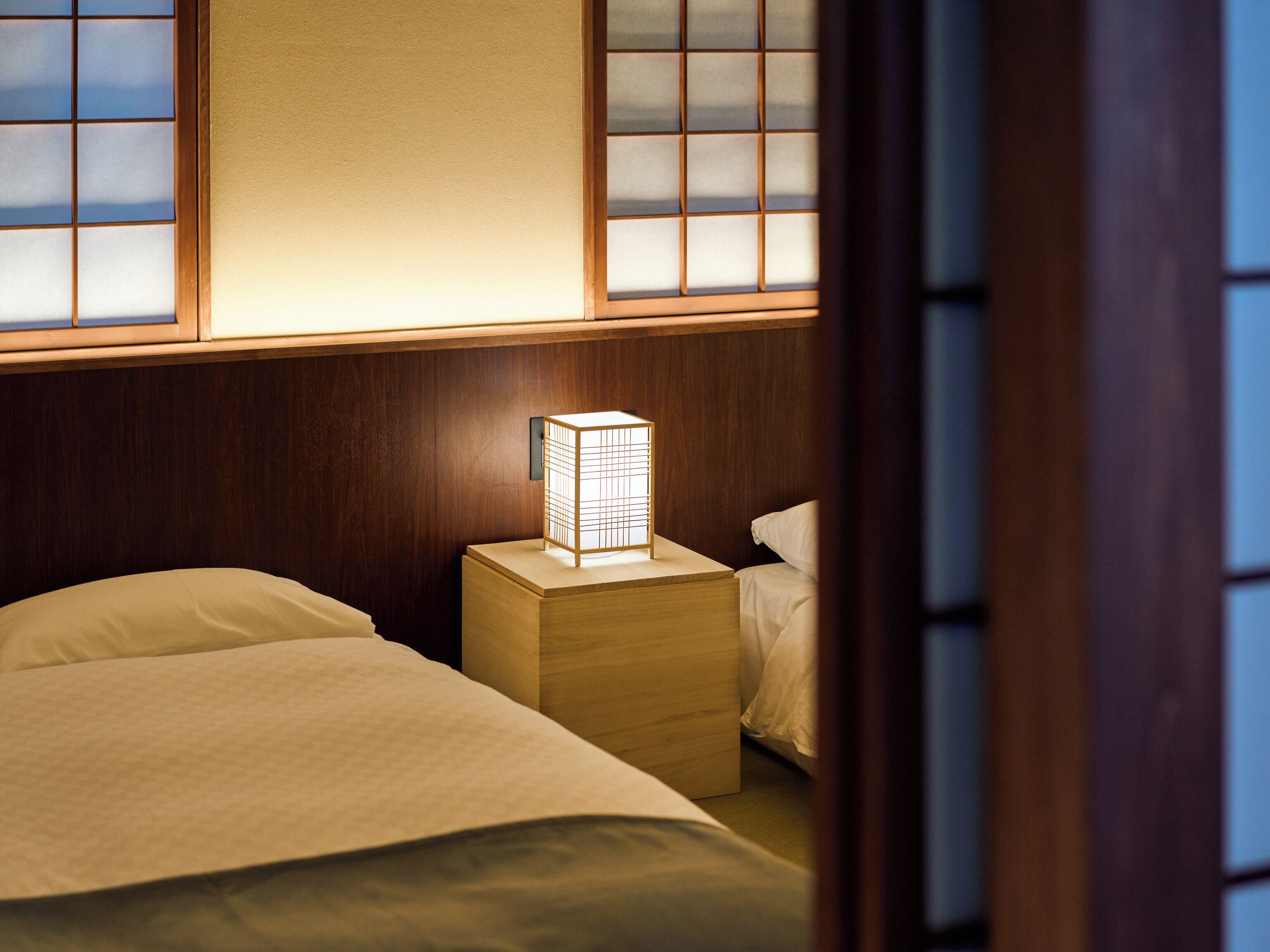 A hotel room with a bed, a nightstand, and a traditional Japanese-style window.