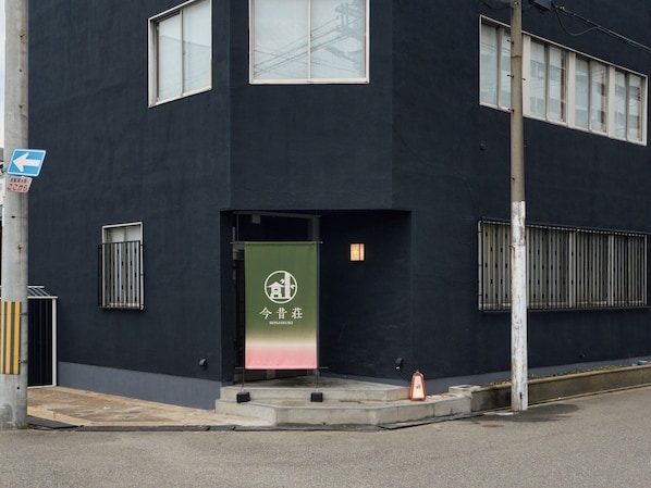 A modern building with a dark facade, a green banner with white text, and a blue directional sign.