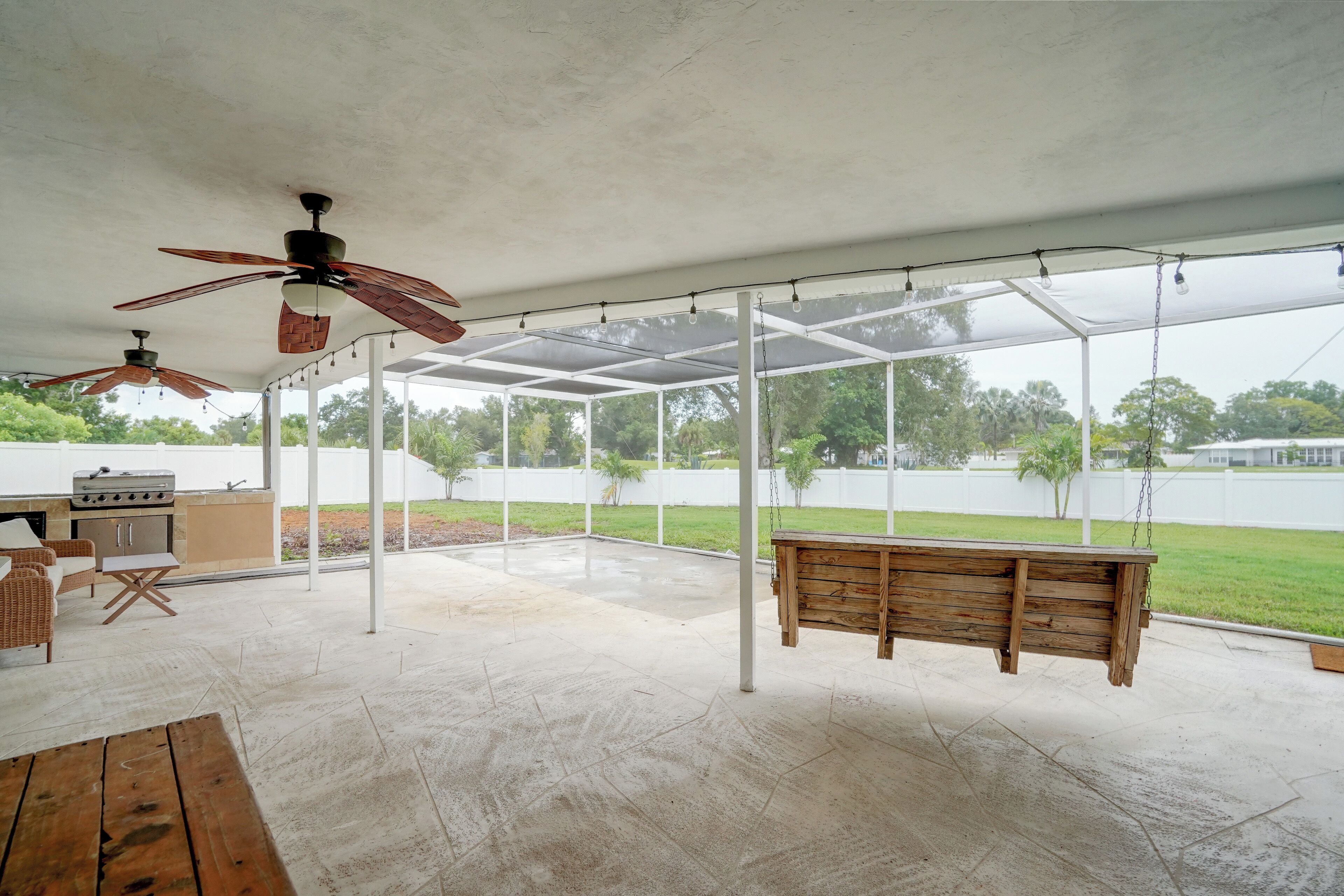 Un patio extérieur couvert, équipé d’un barbecue, de sièges et de ventilateurs de plafond.