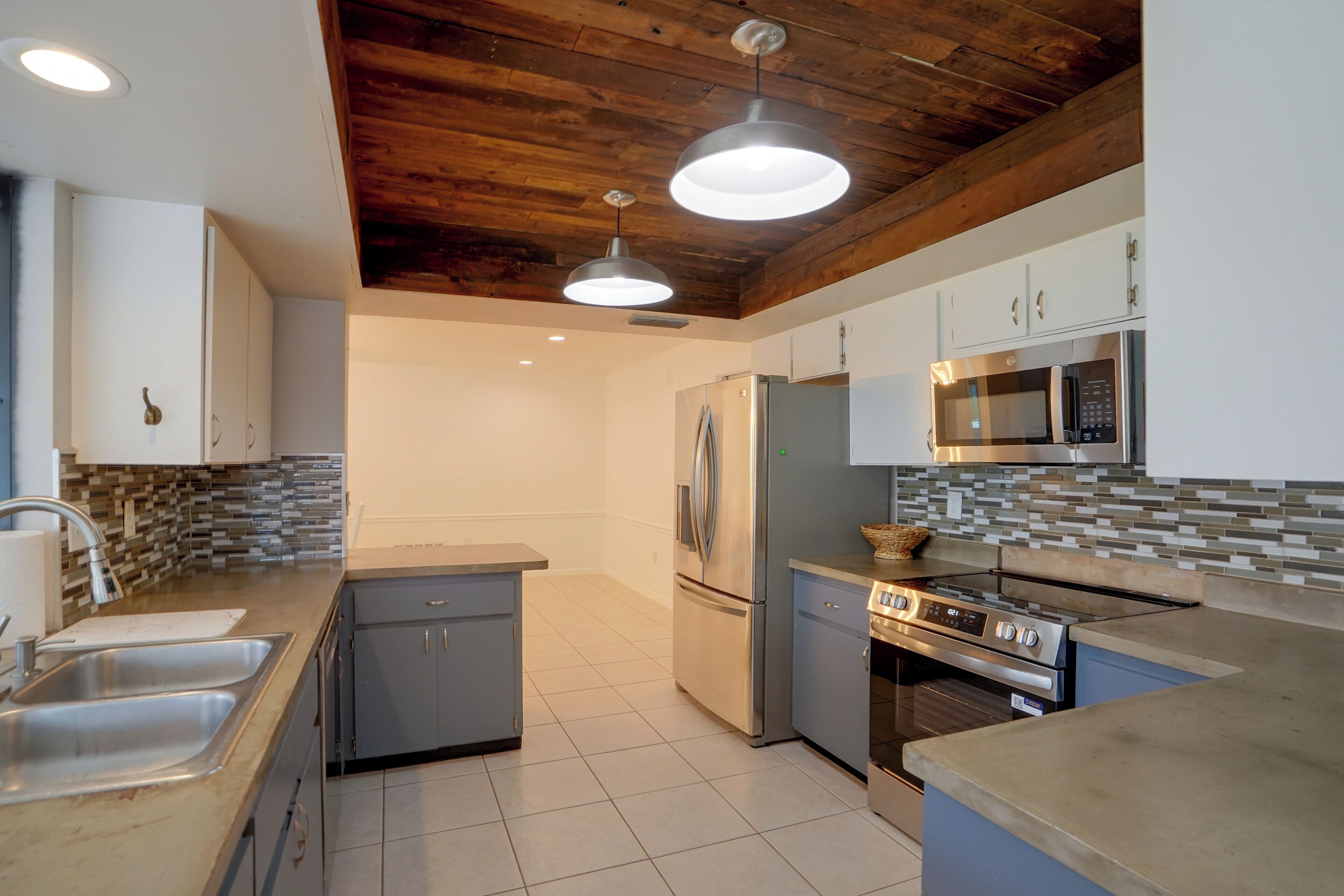 Een moderne keuken met een centraal eiland, roestvrijstalen apparatuur en een houten plafond.