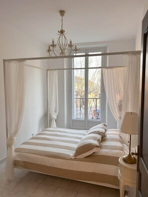 A four-poster bed with a canopy, a chandelier, and a view of the outdoors through a window. - Omnia. Air conditioned charm in historic Frejus. (Fréjus)