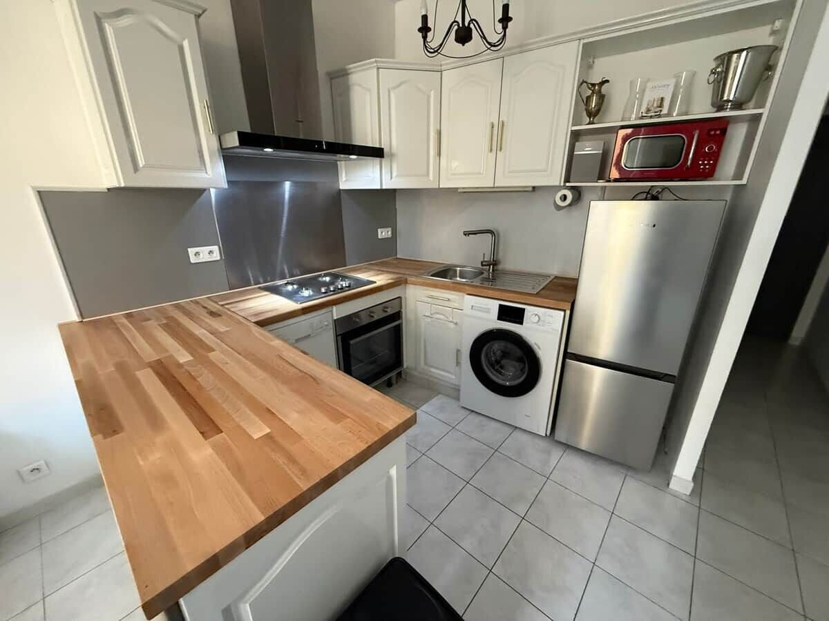 Una cocina compacta con encimera de madera, electrodomésticos de acero inoxidable y armarios blancos.