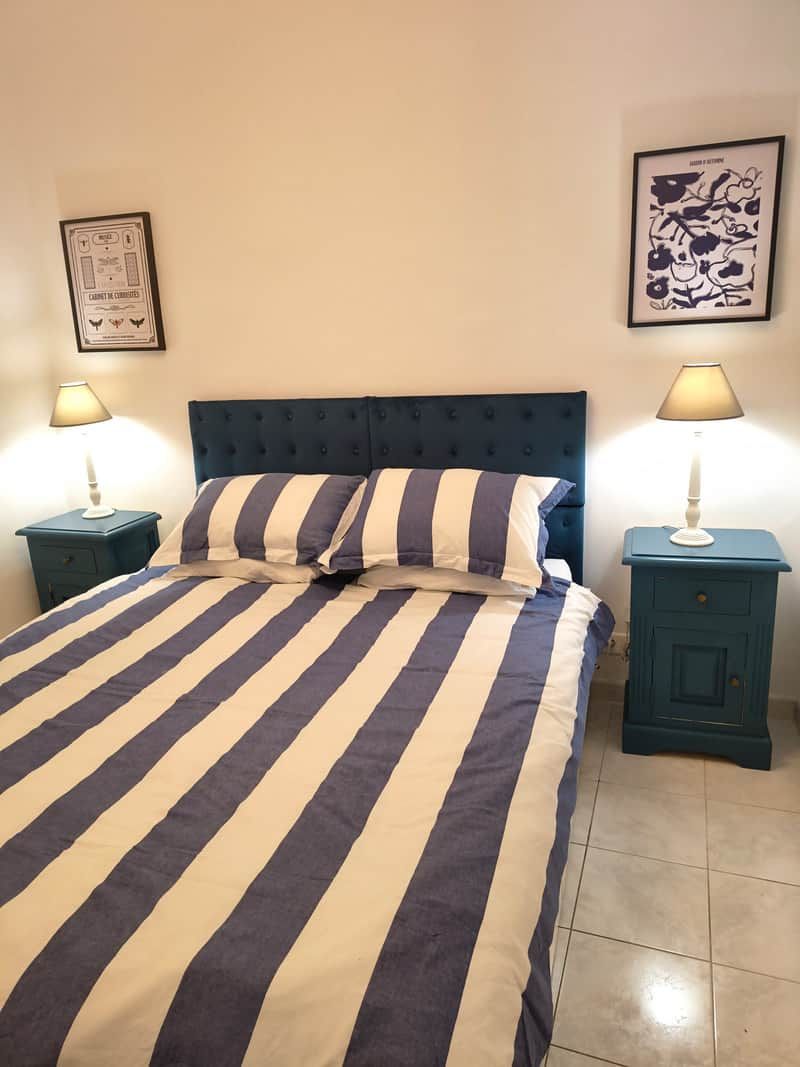 Un lit avec une literie à rayures, deux tables de chevet avec des lampes et des œuvres d’art murales.