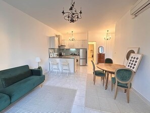 A modern living room with a green sofa, a dining area with a wooden table and chairs, and a kitchen in the background. - Omnia. Air conditioned charm in historic Frejus. (Fréjus)