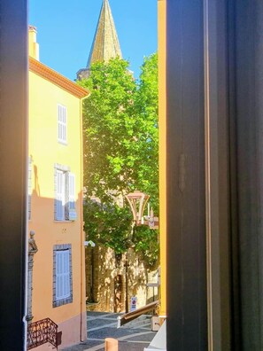 A narrow street with a church spire in the background, a street lamp, and a building with shutters. - Omnia. Air conditioned charm in historic Frejus. (Fréjus)