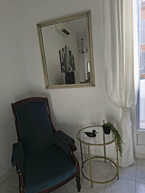 A room with a dark green armchair, a round gold-framed side table with a plant, and a large mirror on the wall. - Omnia. Air conditioned charm in historic Frejus. (Fréjus)