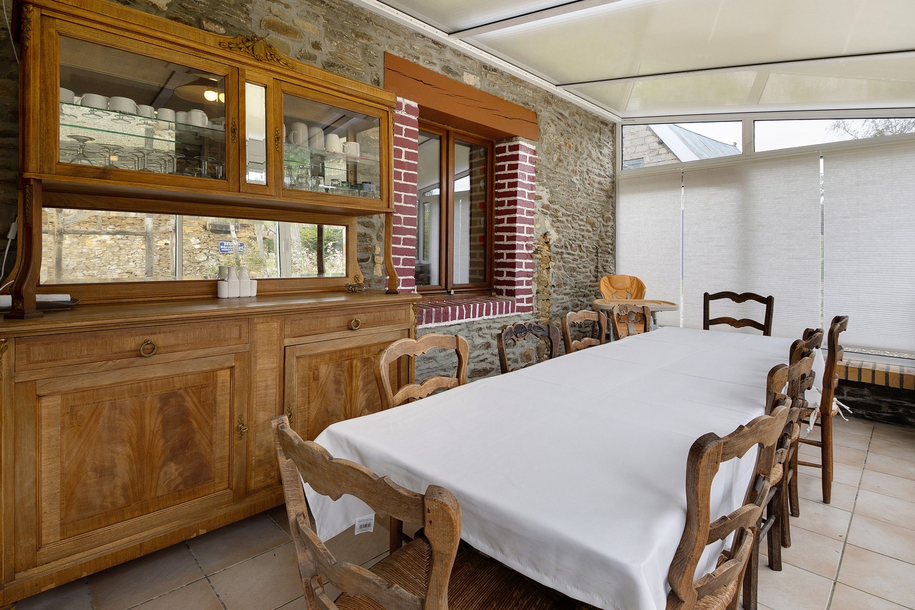 A dining area with a long table, wooden chairs, a cabinet with glass doors, and a brick wall.