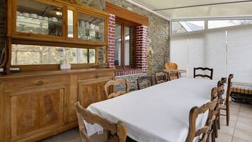 A dining area with a long table, wooden chairs, a cabinet with glass doors, and a brick wall.
