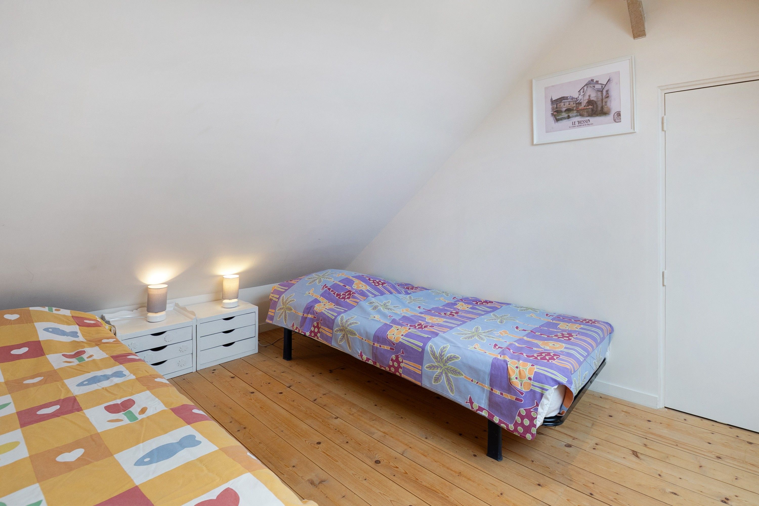 Ein Schlafzimmer mit einem Bett, einem Nachttisch, einer Lampe, einem Wandbild und Holzboden.