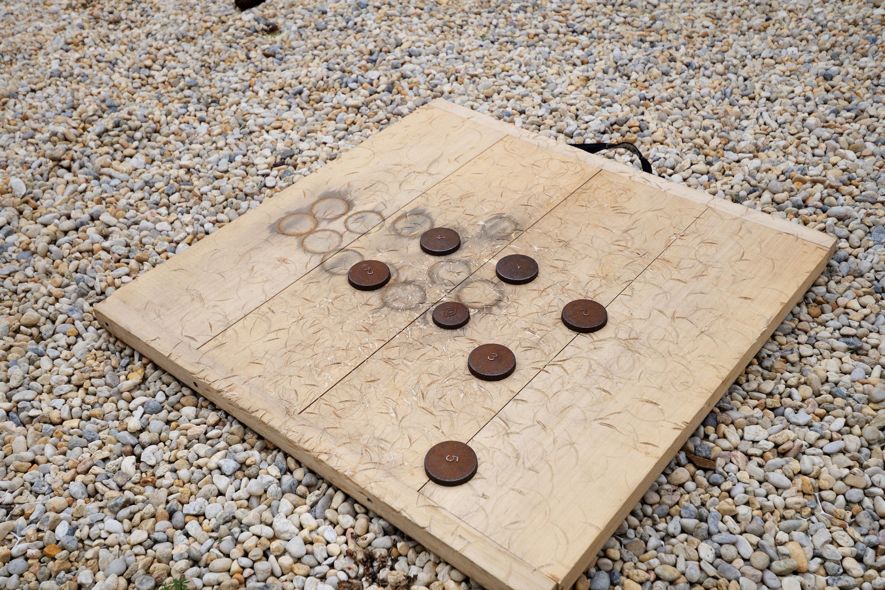 A wooden board with circular tokens on a pebbled surface.