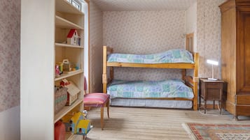 Une chambre d’enfant avec un lit superposé, une armoire en bois, un petit bureau et une bibliothèque remplie de jouets et de livres.