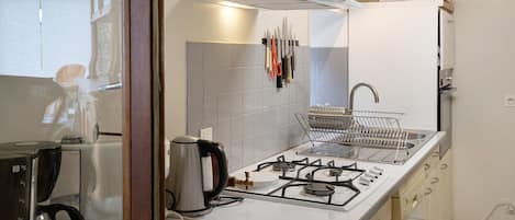 Una cocina compacta con estufa a gas, hervidor y pileta.