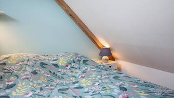 Une chambre avec un plafond en pente, un lit recouvert d’une couvre-lit à motifs floraux, une lampe de chevet et une table de chevet.
