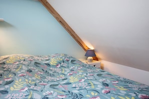 Ein Schlafzimmer mit schrägen Wänden, einem Bett mit Blumenmuster, einer Nachttischlampe und einem Nachttisch.