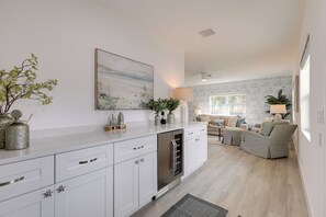 Eine moderne Küche mit weißen Schränken, einem Edelstahl-Kühlschrank und Dekoration. Es gibt einen Essbereich mit Tisch und Stühlen sowie ein Wohnzimmer mit Sofa und Lampe.