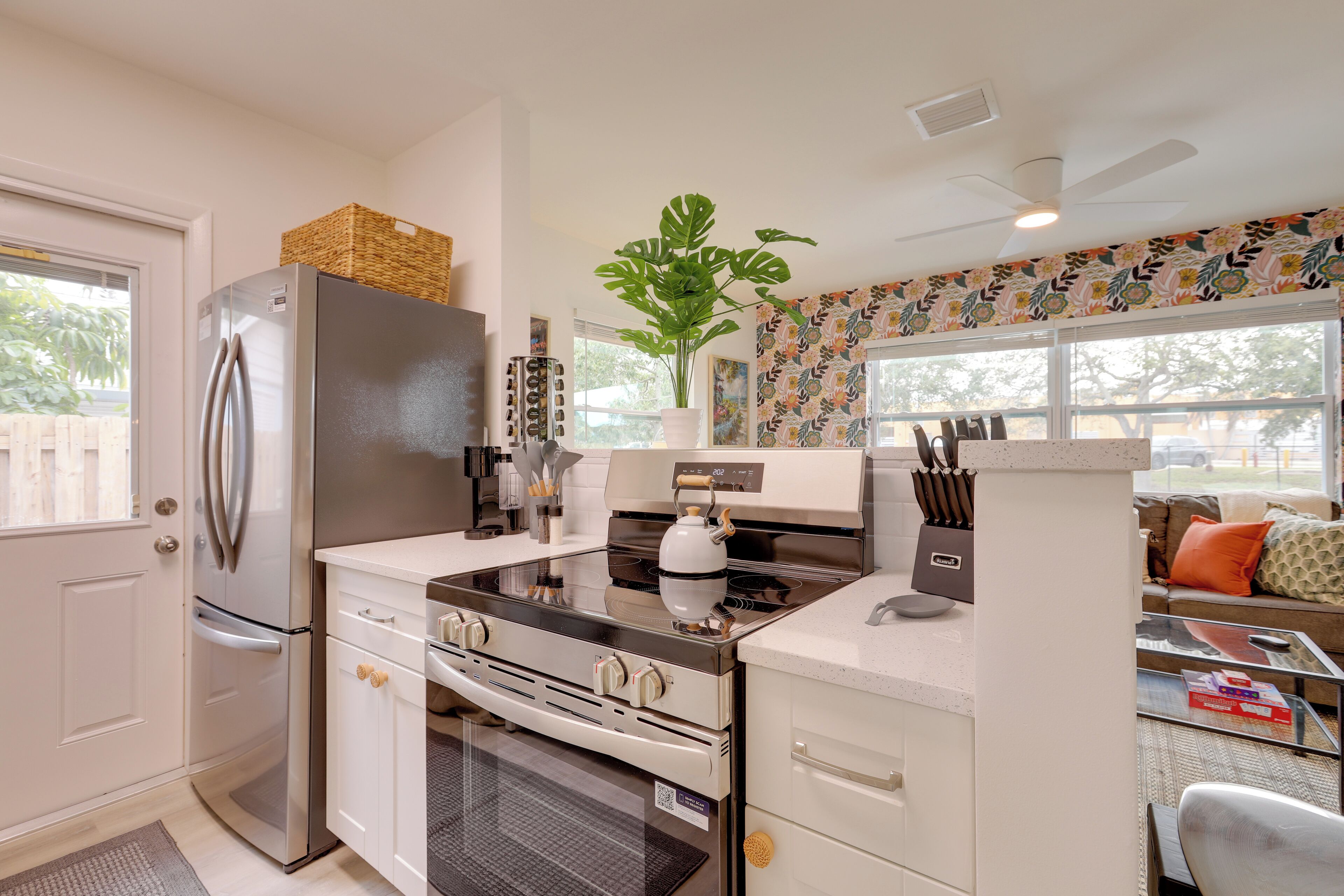 A compact kitchen with a refrigerator, oven, and stove, a potted plant, and a window with a view of the outdoors.