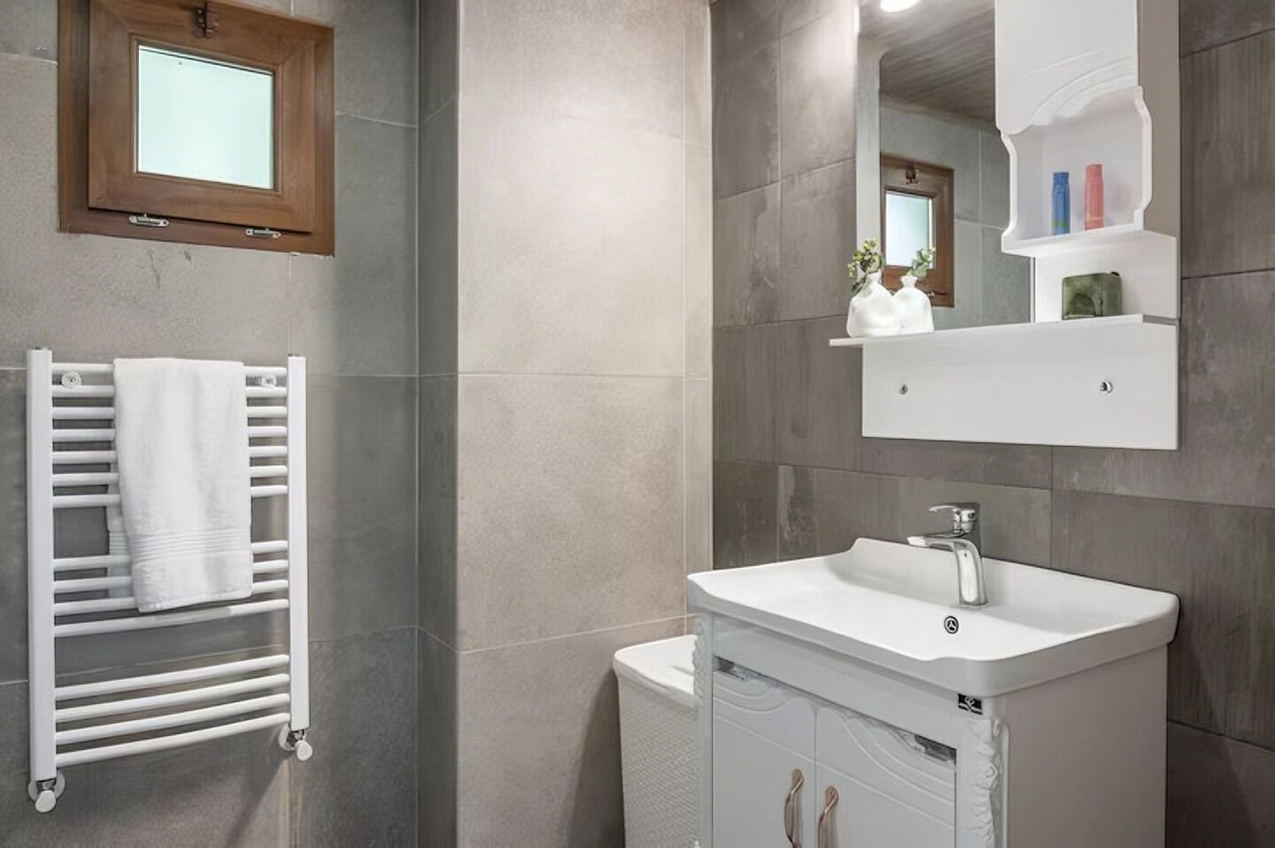 Une salle de bain avec un lavabo blanc, un porte-serviettes et un miroir doté d’étagères au-dessus.