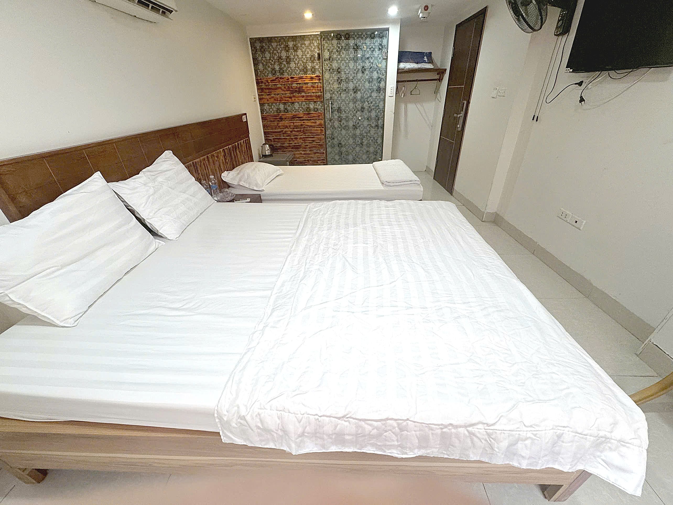 A hotel room with two beds, a television mounted on the wall, and a bathroom with a shower and a towel rack.
