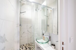 A bathroom with a glass shower enclosure, a glass sink, and a tiled floor. - Charming and Bright 1BDR Near the Marais (Paris)
