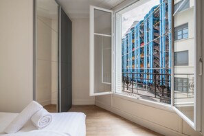 A hotel room with a large window, a bed, and a view of industrial structures outside. - Charming and Bright 1BDR Near the Marais (Paris)