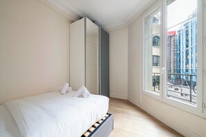 Ein Schlafzimmer mit einem Bett, einem großen Spiegel und Blick auf eine Baustelle durch ein Fenster.