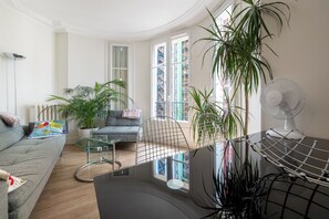 Ein Wohnzimmer mit einer Couch, einem Glastisch, einem Sessel und einer Zimmerpflanze.