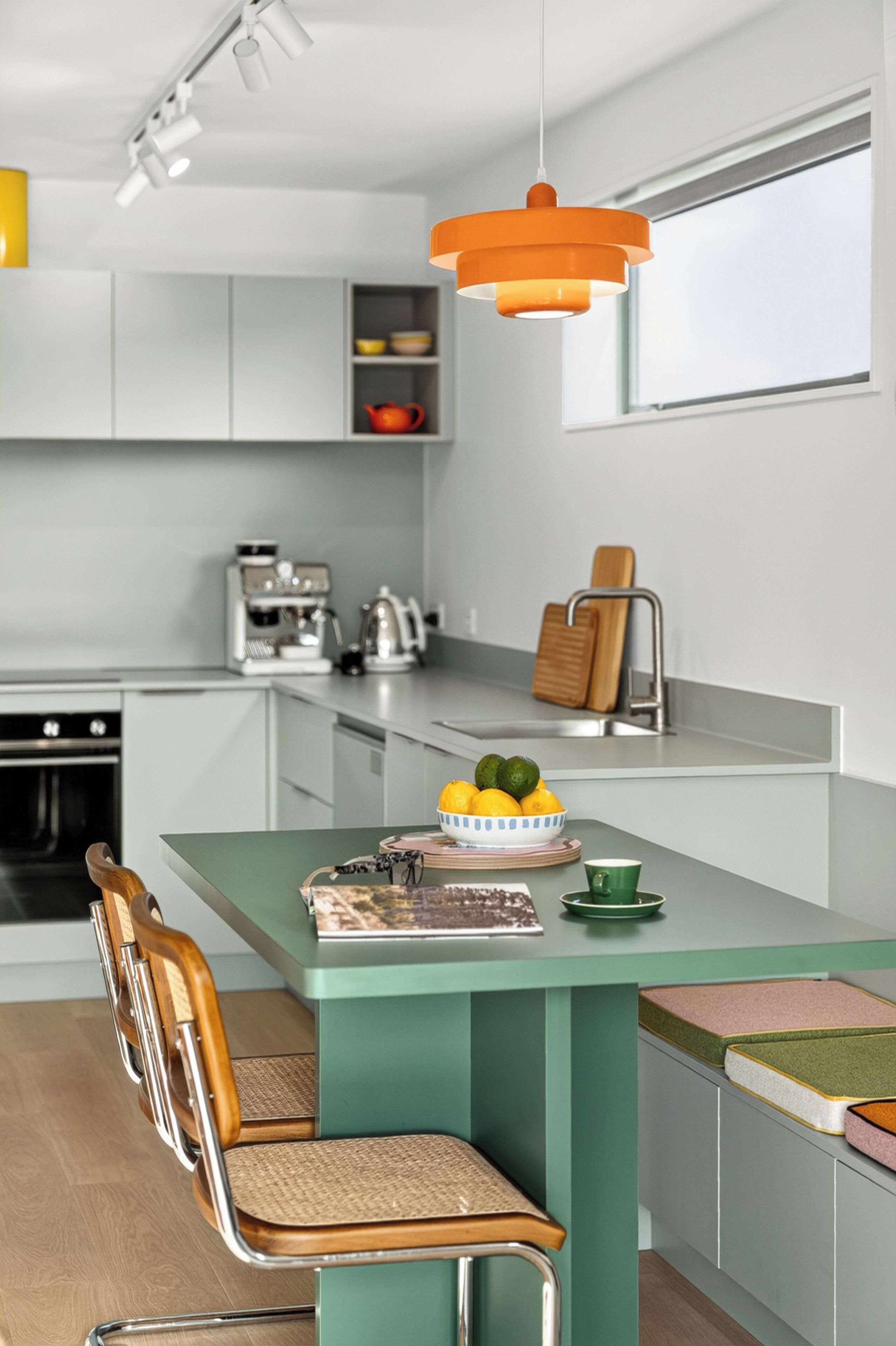 Eine moderne Küche mit einer zentralen Kochinsel, einer Kaffeemaschine und einer hängenden, orangefarbenen Pendelleuchte.