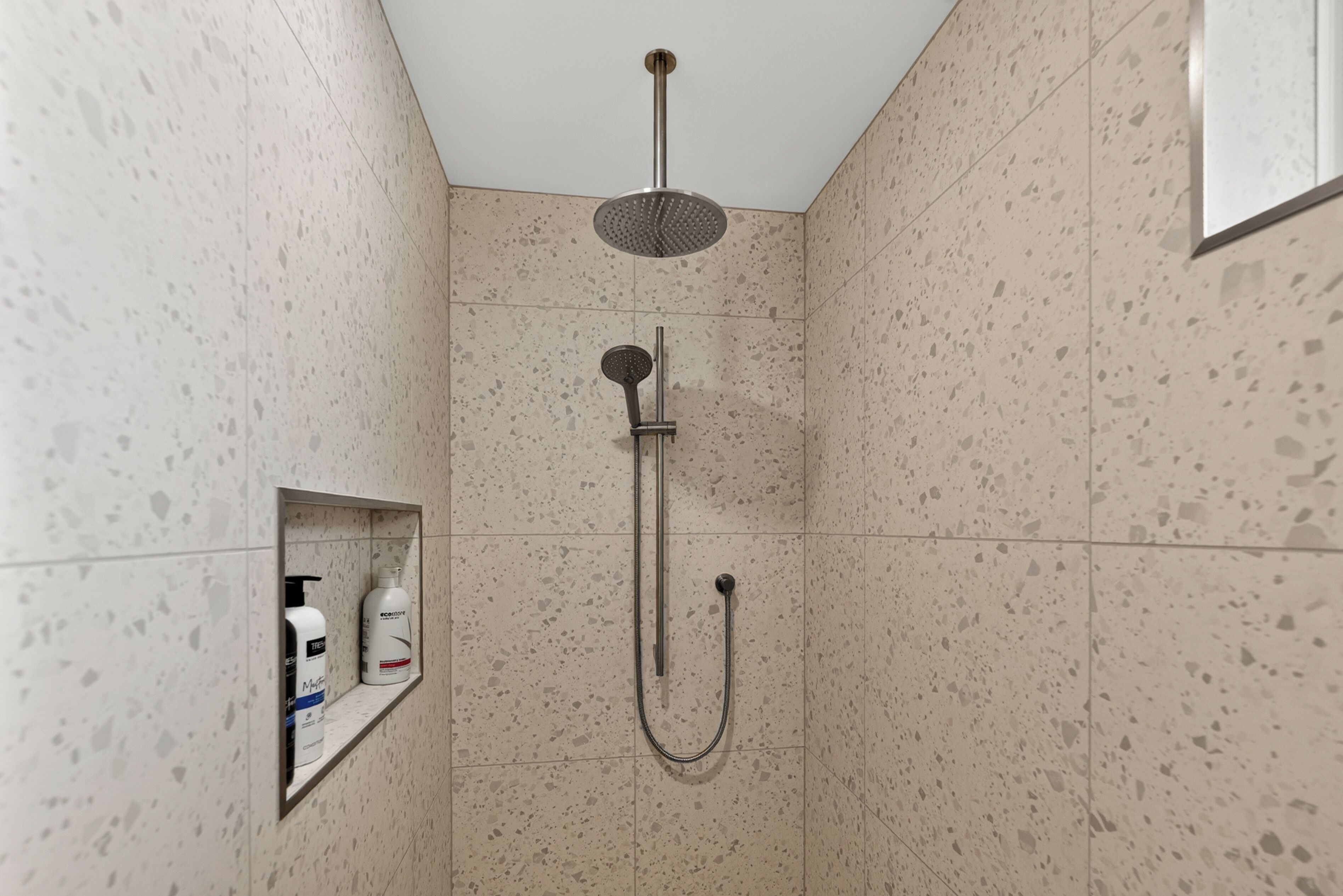 A shower with a handheld showerhead and a wall-mounted rain showerhead.