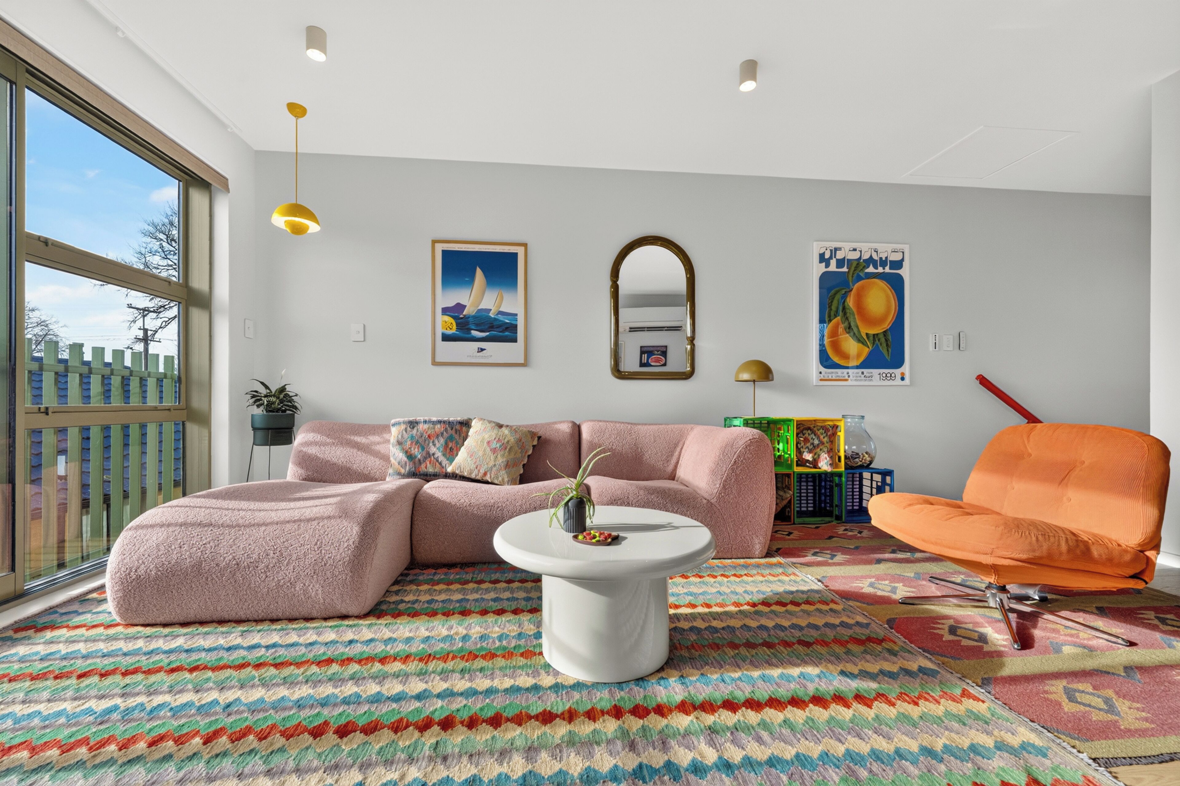 A modern living room with a sectional sofa, a coffee table, a colorful rug, a large window, and artwork on the walls.