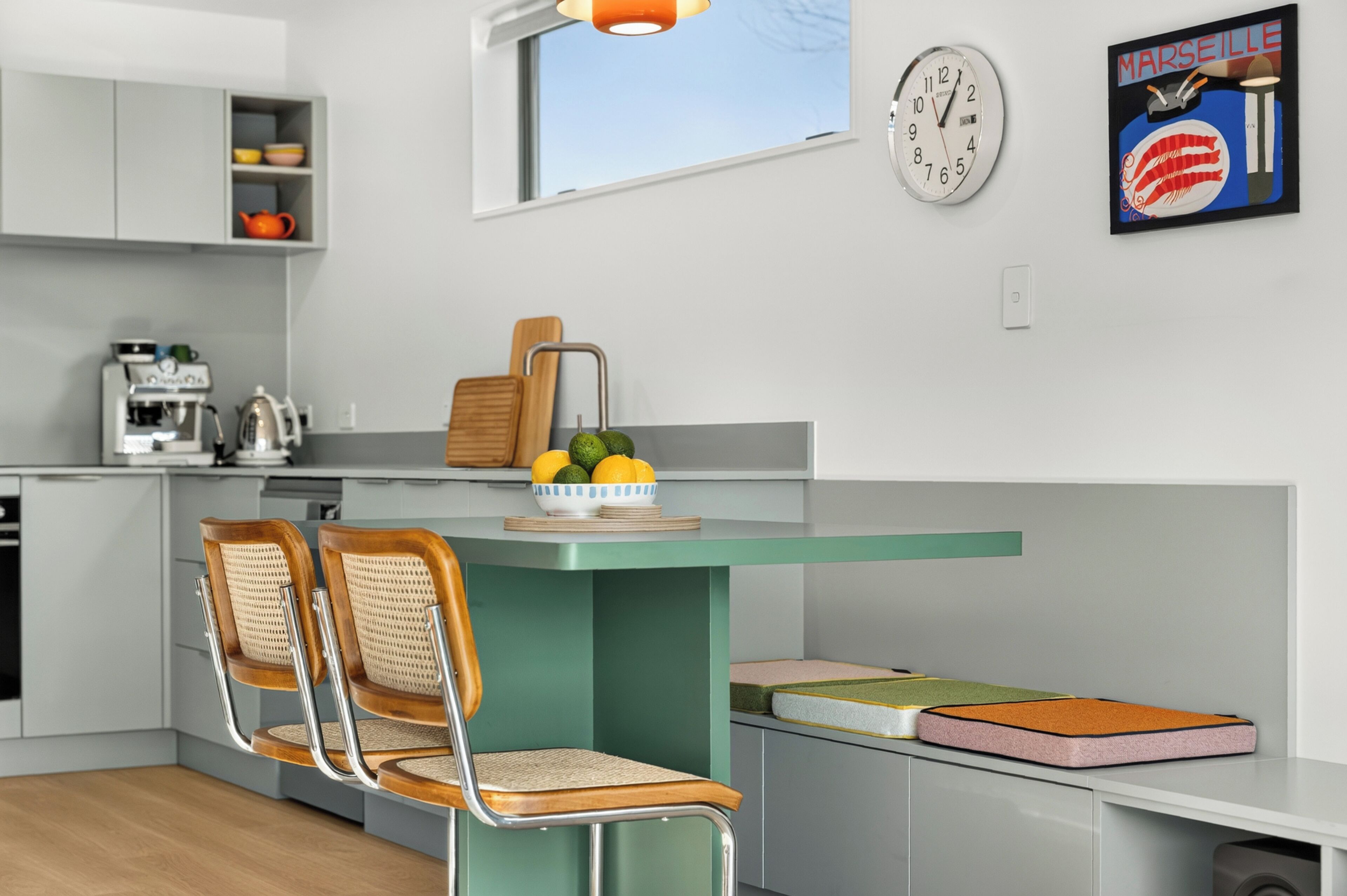 A modern kitchen with a green island, two chairs, a coffee machine, and a clock on the wall.