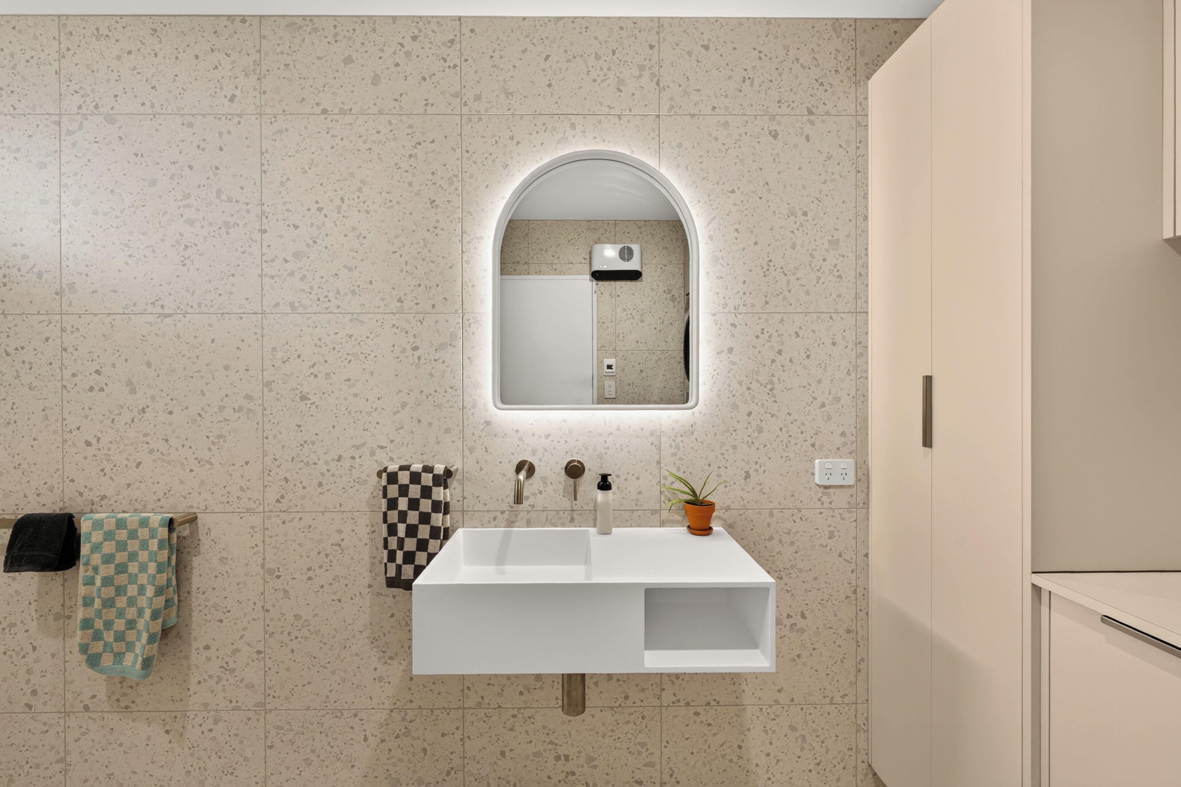 A bathroom with a white sink, a mirror with an arch, and a towel rack with two towels.