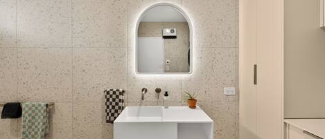 A bathroom with a white sink, a mirror with an arch, and a towel rack with two towels.