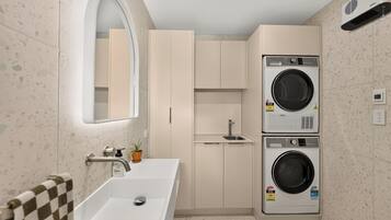 A modern bathroom with a sink, mirror, cabinets, and two stacked washing machines.