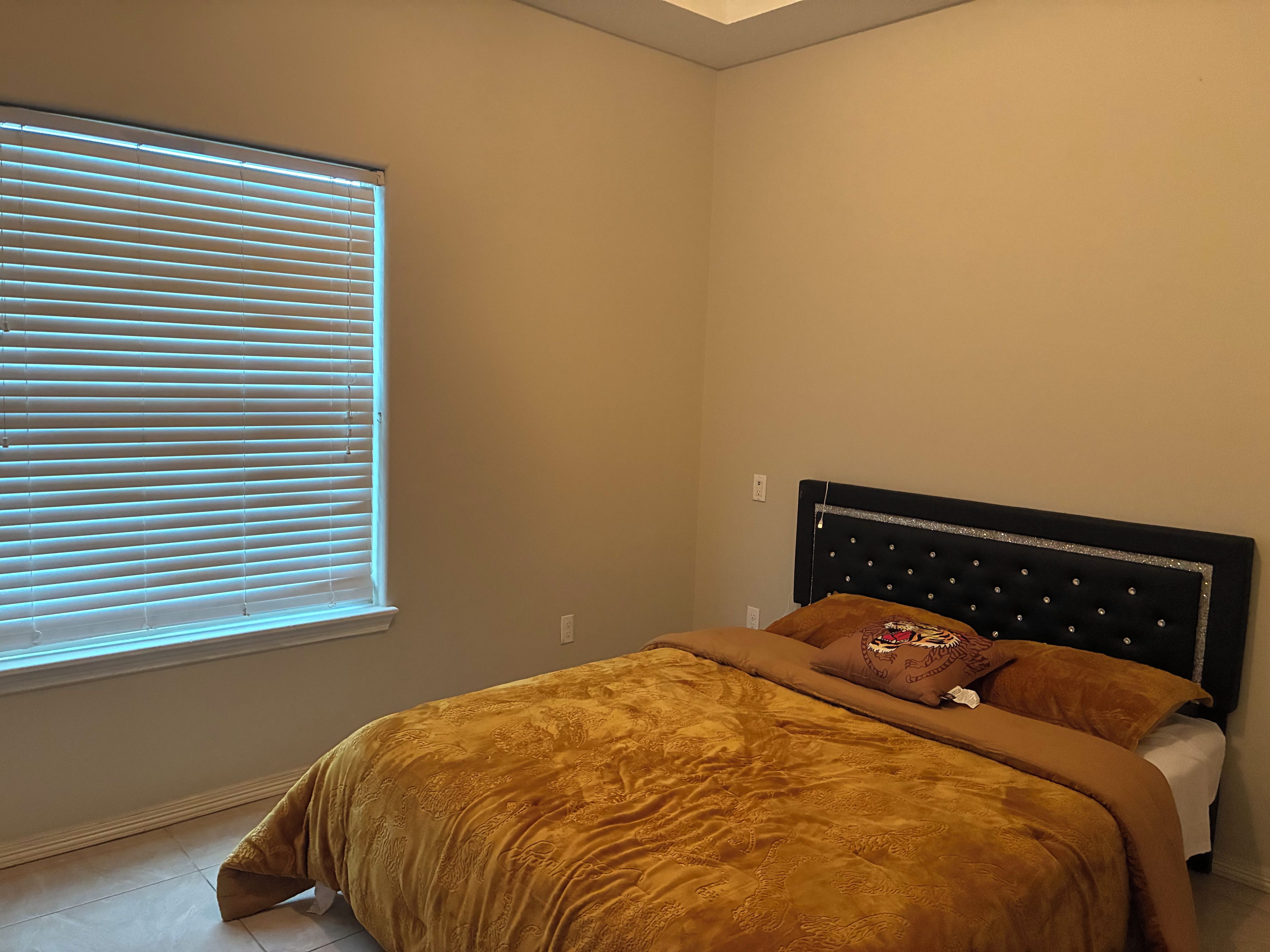 A bedroom with a bed, a window with blinds, and a headboard with a decorative panel.
