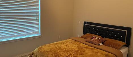 A bedroom with a bed, a window with blinds, and a headboard with a decorative panel.