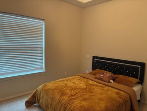 A bedroom with a bed, a window with blinds, and a headboard with a decorative panel.