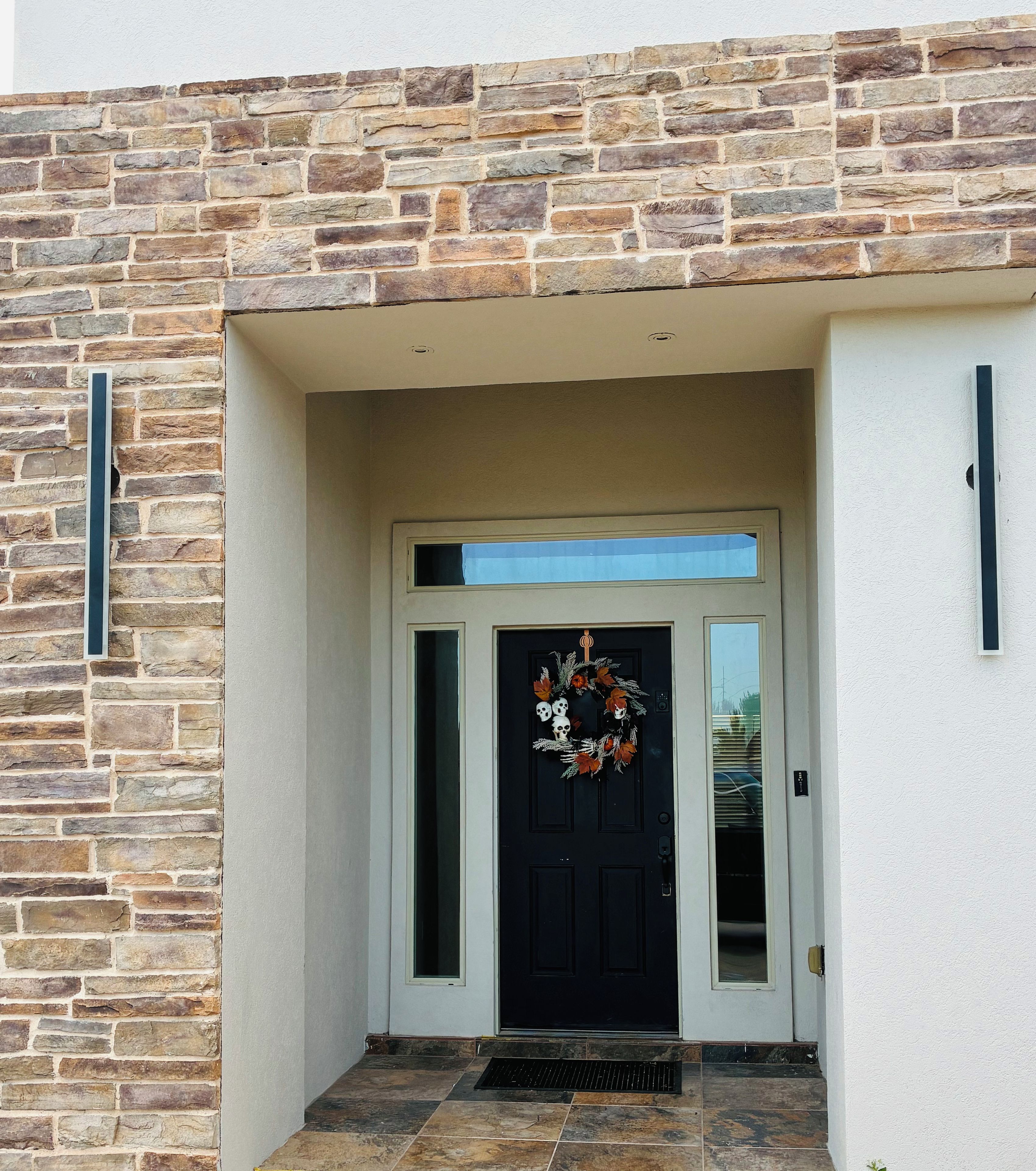 Ingresso con facciata in pietra, una porta nera e un piccolo oblò sopra la porta, con un gradino in metallo che conduce all'ingresso.