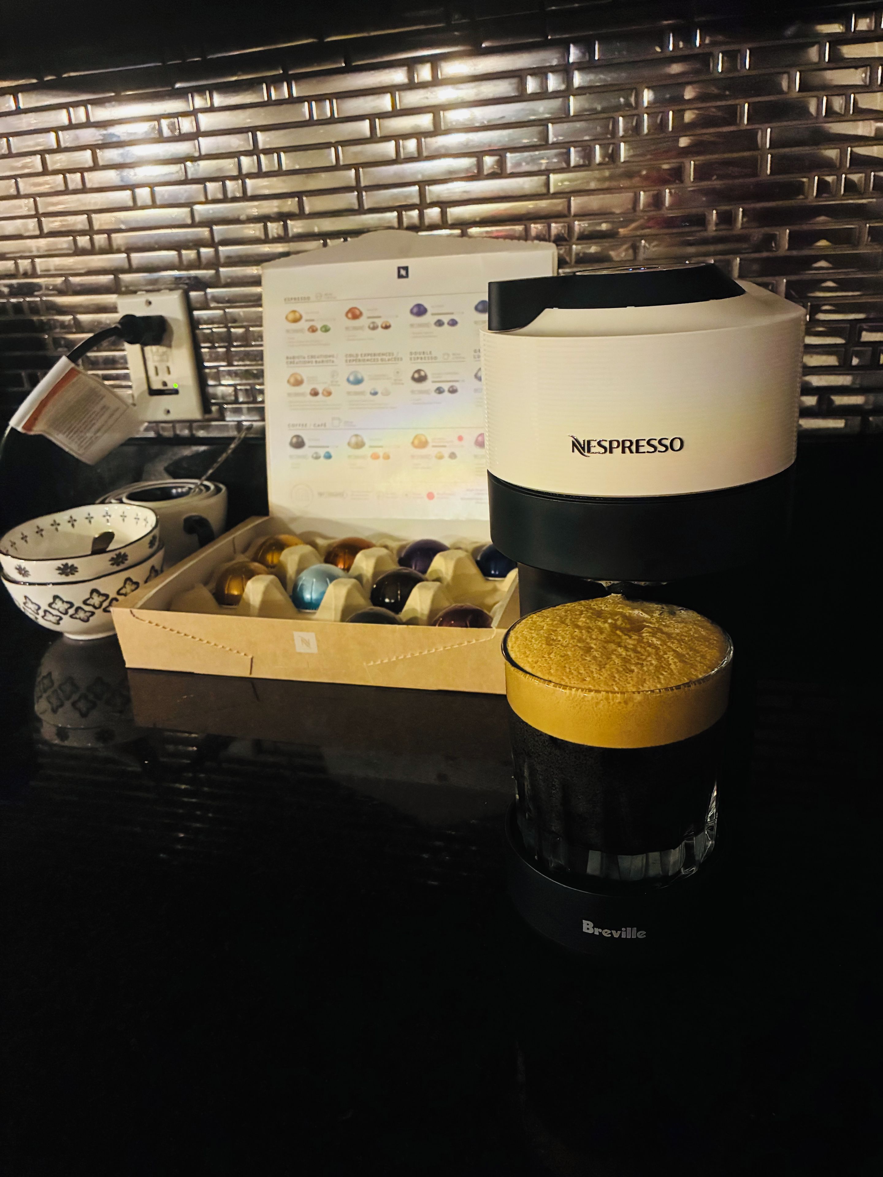 Een koffieapparaat, een doos koffiecups, een kop koffie en een Breville koffiemachine op een aanrecht.