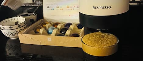 Een koffieapparaat, een doos koffiecups, een kop koffie en een Breville koffiemachine op een aanrecht.