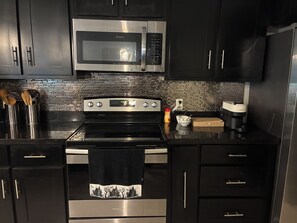 A modern kitchen with stainless steel appliances, black cabinets, and a tiled backsplash.