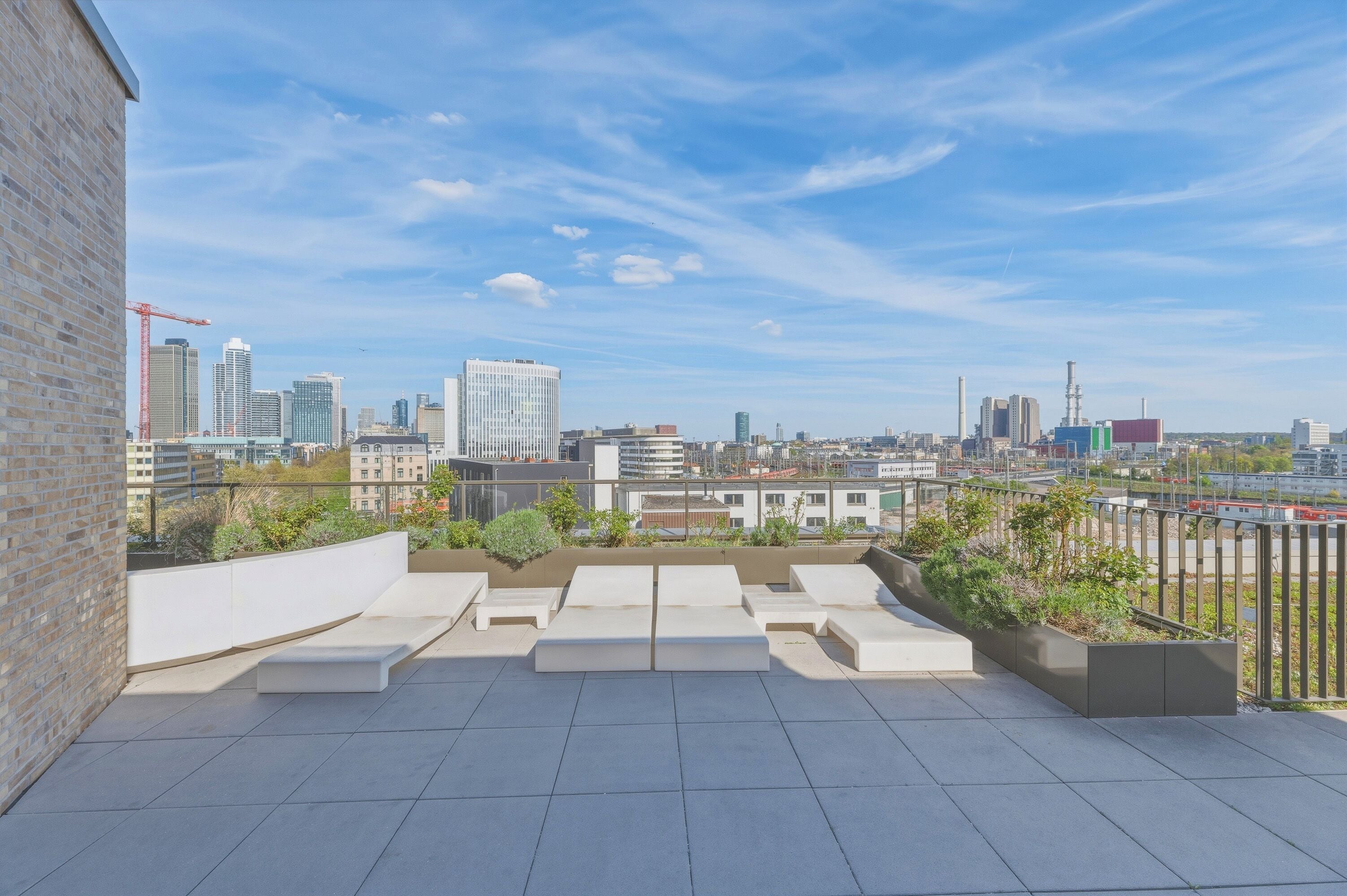 Eine Dachterrasse mit Blick auf eine Stadtlandschaft, mit einer Mischung aus modernen und älteren Gebäuden und blauem Himmel.