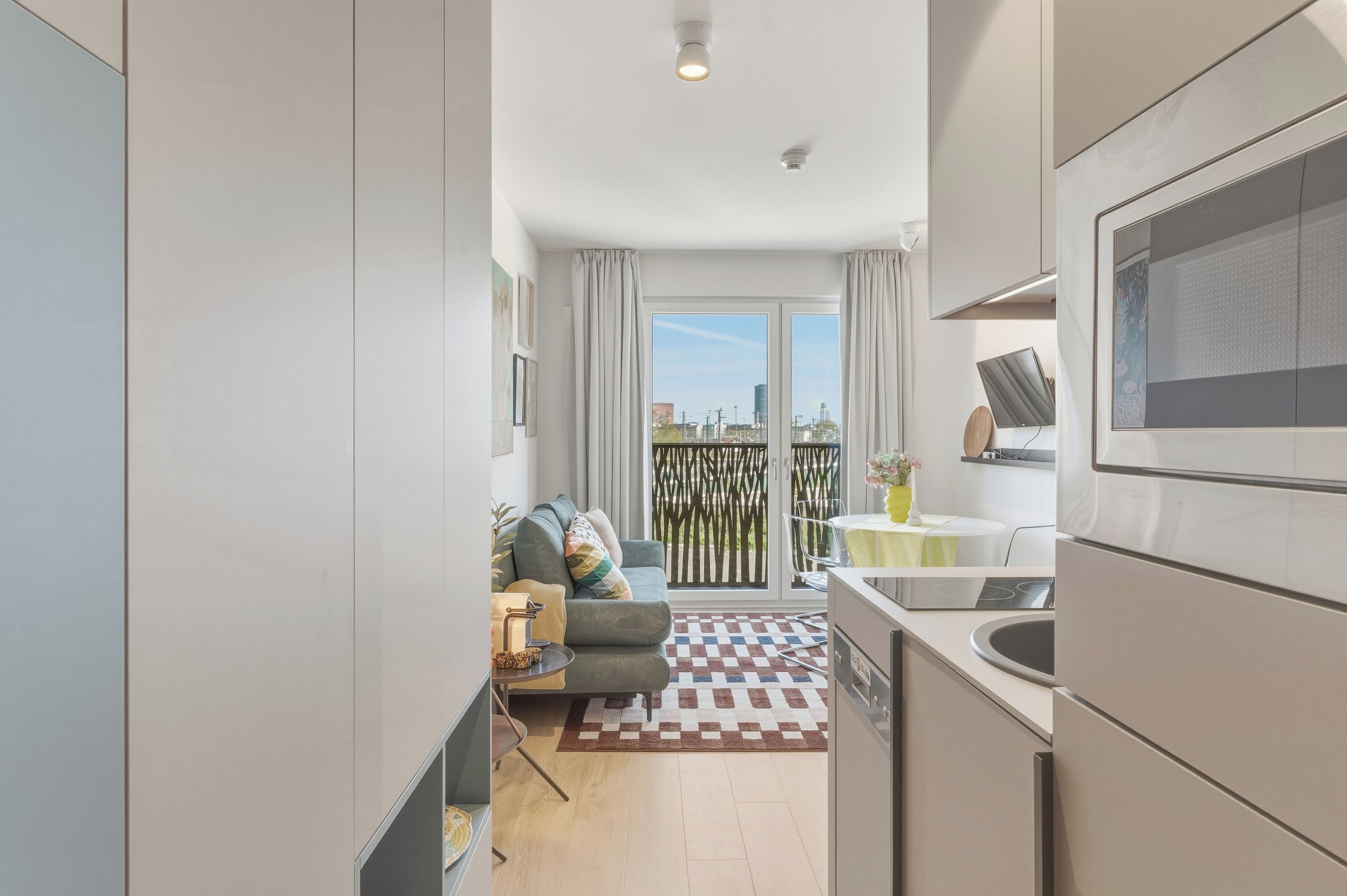 A modern kitchen with a dining area, a sofa, and a view of the city through large windows.