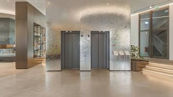 A modern lobby with two elevators, a reception desk, and a staircase.