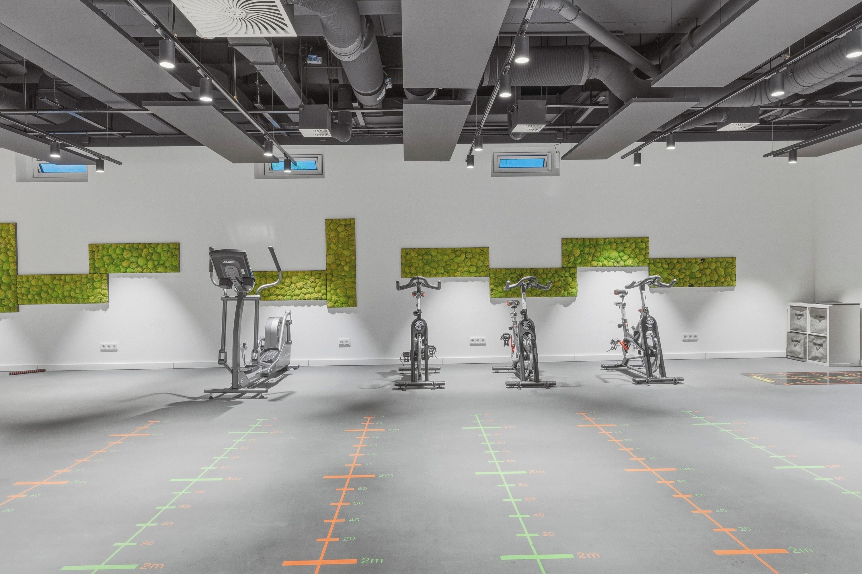 A gym with exercise equipment, green wall panels, and a floor with measurement markings.