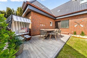 A brick house with a wooden deck, outdoor seating, and paddleboards on the wall. - Sylter Herzstück - Modern 3-room vacation apartment with approximately 75 m² of living space, for (Wenningstedt-Braderup (Sylt))