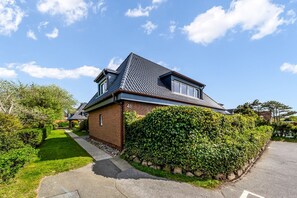 Ein zweistöckiges Haus mit geneigtem Dach, einer Ziegel-Fassade und einem gepflegten Garten.