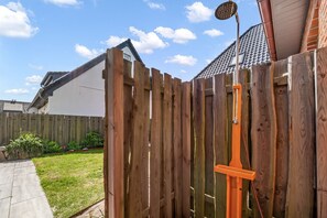 Ein Holzzaun mit daran befestigter Metallkonstruktion, ein klarer Himmel und ein Haus mit Ziegeldach im Hintergrund.
